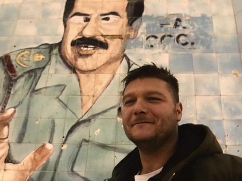 Woolley poses in front of a defaced mural of Saddam Hussein in Baghdad while covering the Iraq War in 2005.